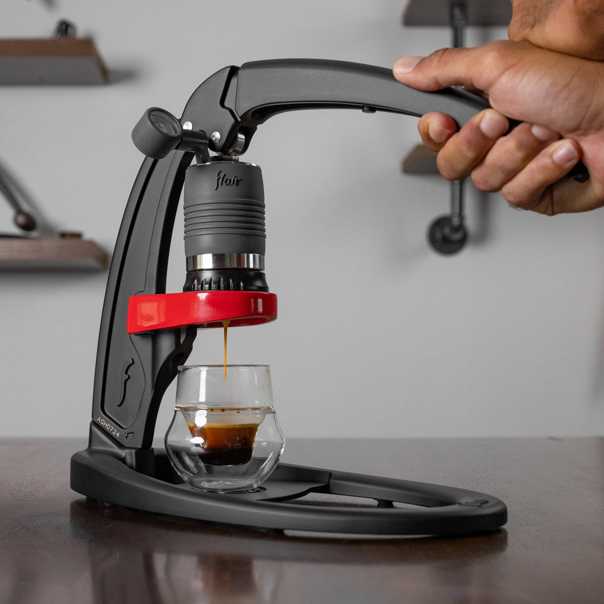 Flair Classic manual espresso maker on a dark counter brewing espresso with hands on the lever.