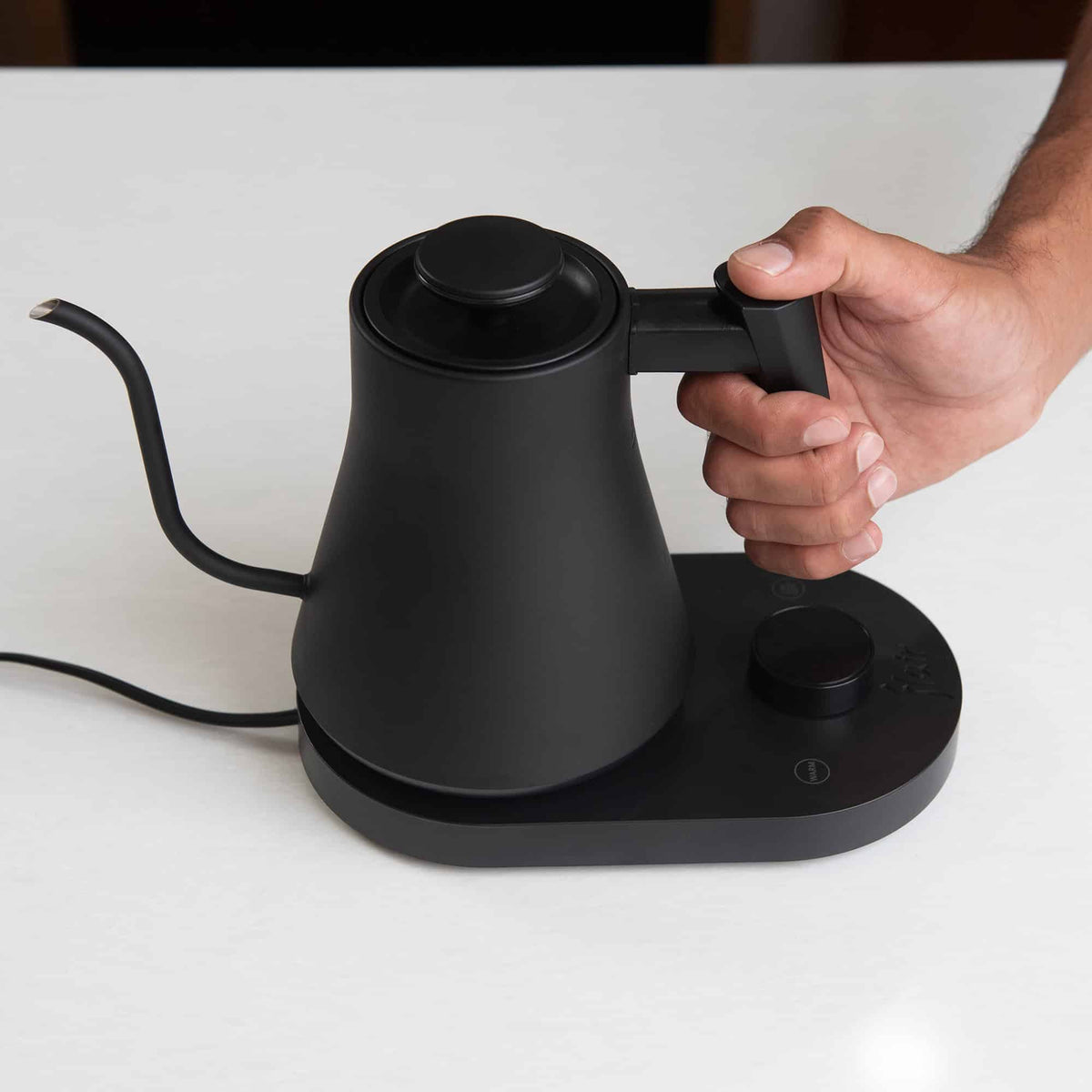 The Flair digital gooseneck kettle on a white countertop with a mans hand on the handle.