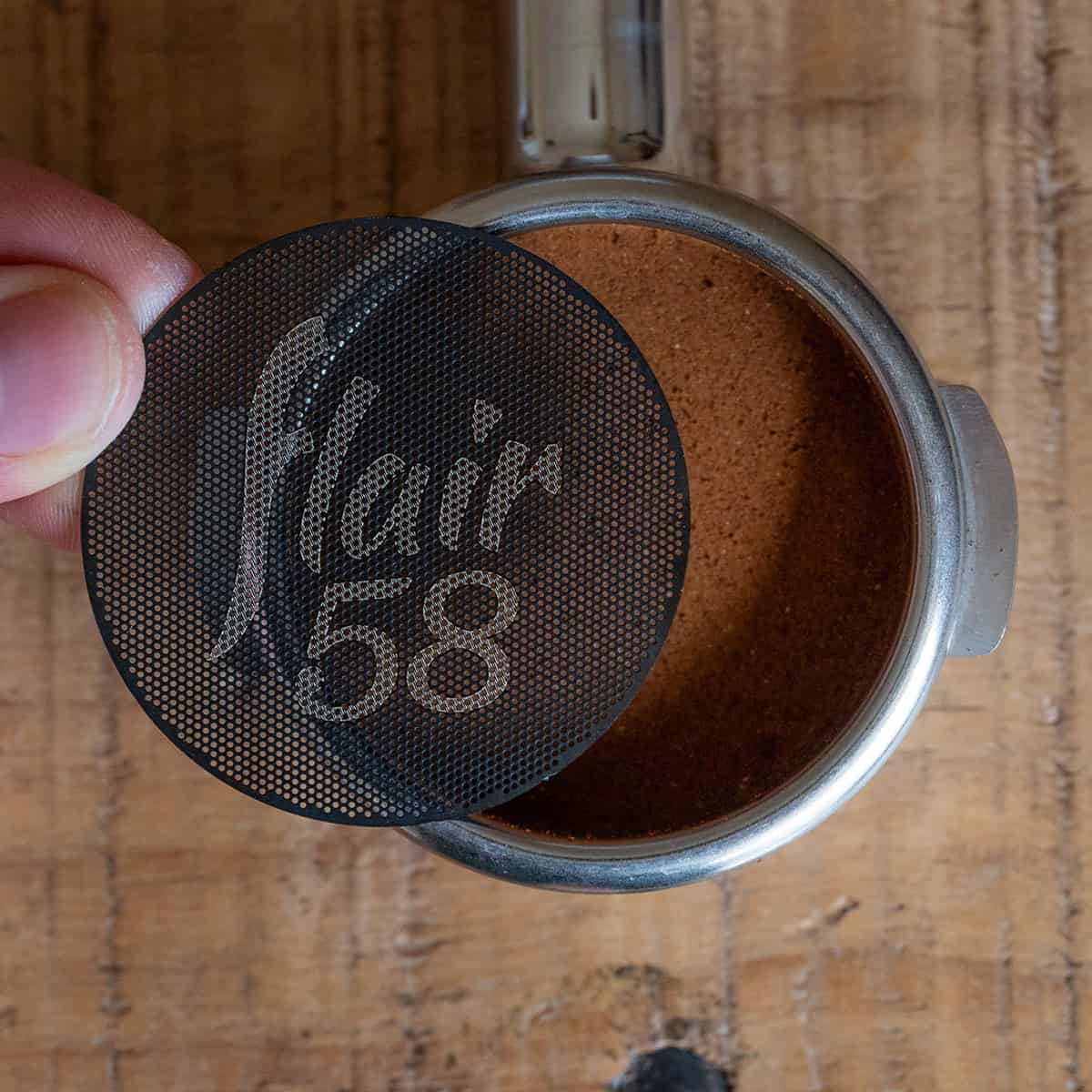 Flair 58 etched puck screen being added to the top of a bed of coffee grounds