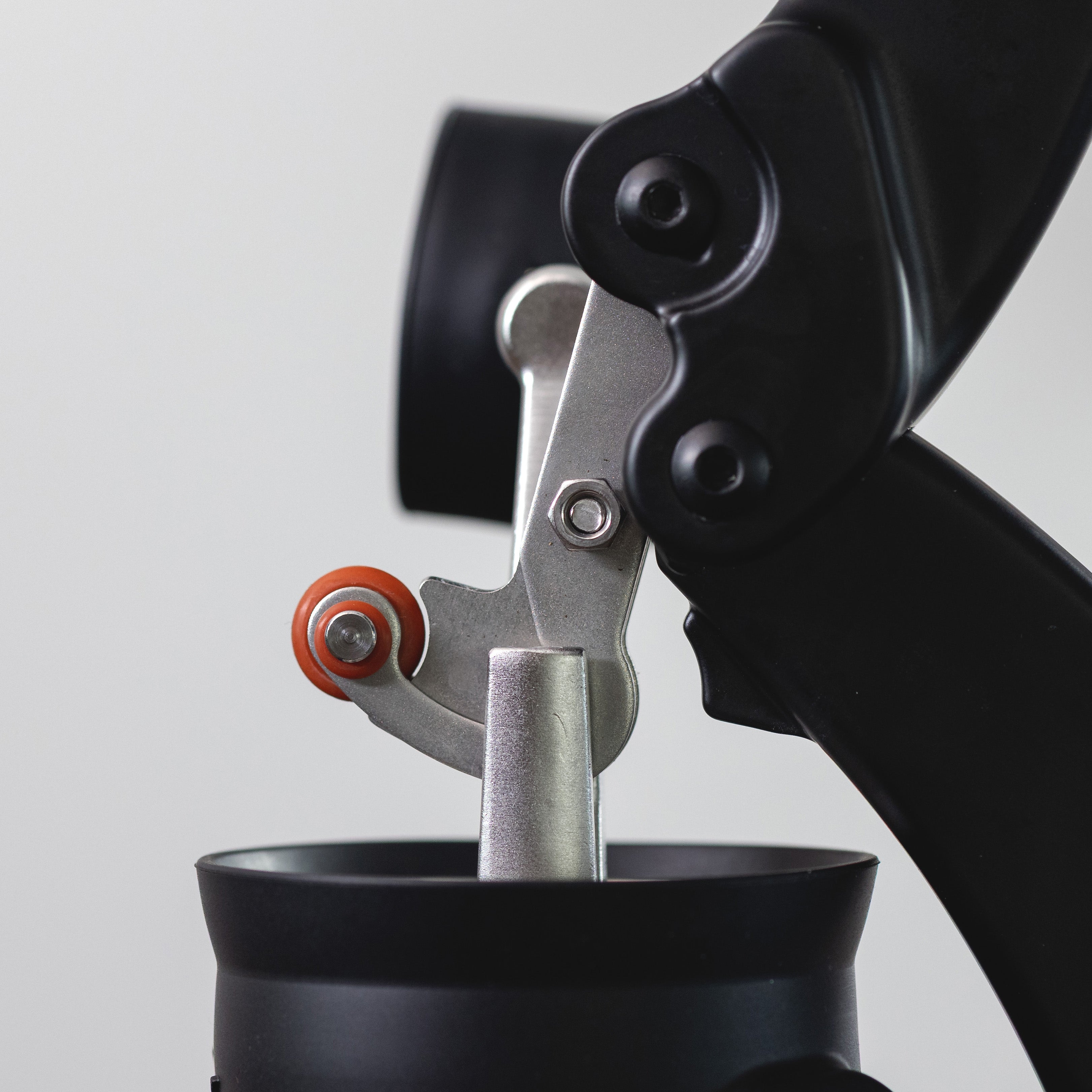 Close-up of a black and silver crank with a small orange wheel, shown against a light gray background.