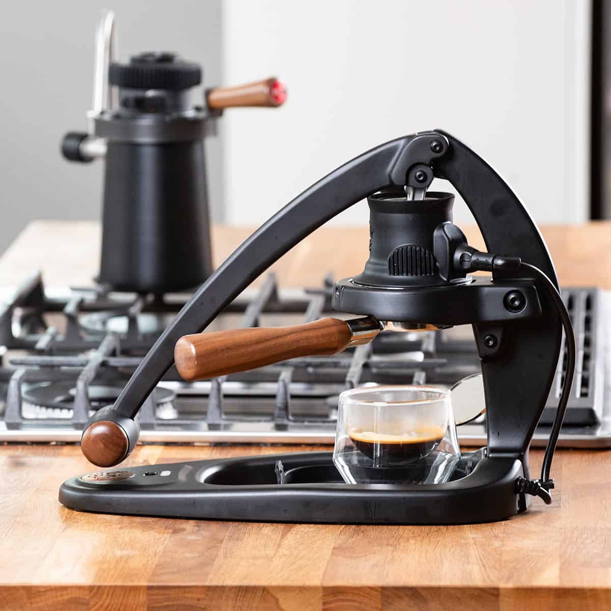 Manual espresso grinder with a glass of freshly brewed espresso on a kitchen counter.