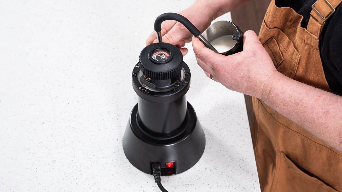 Person using a black coffee grinder on a white surface