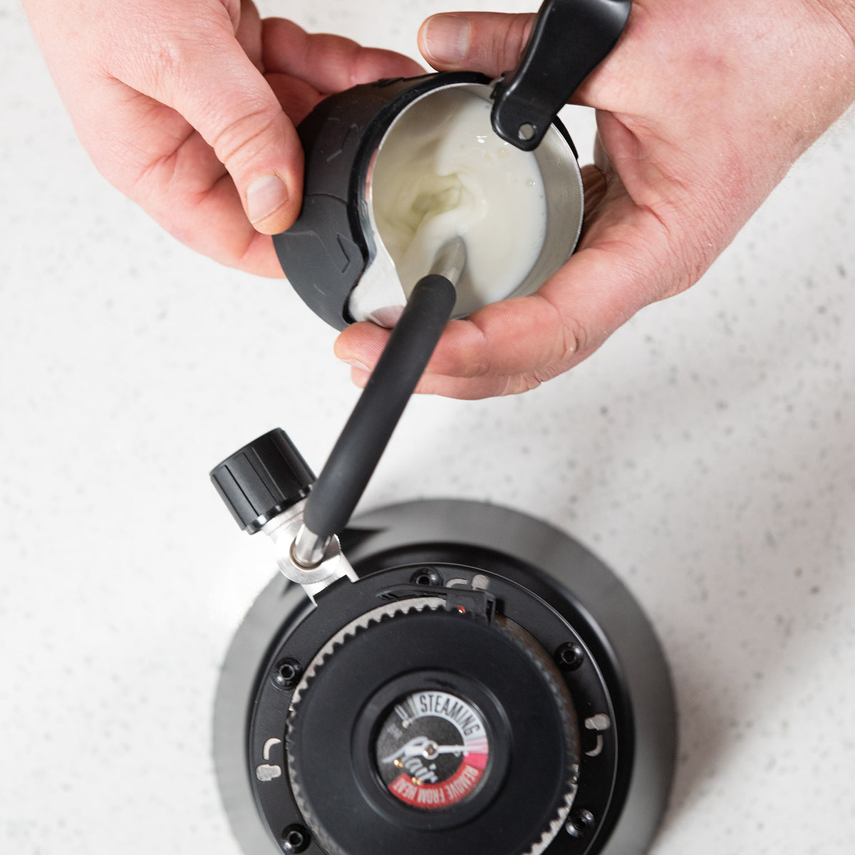 Person using a handheld steaming device on a white surface