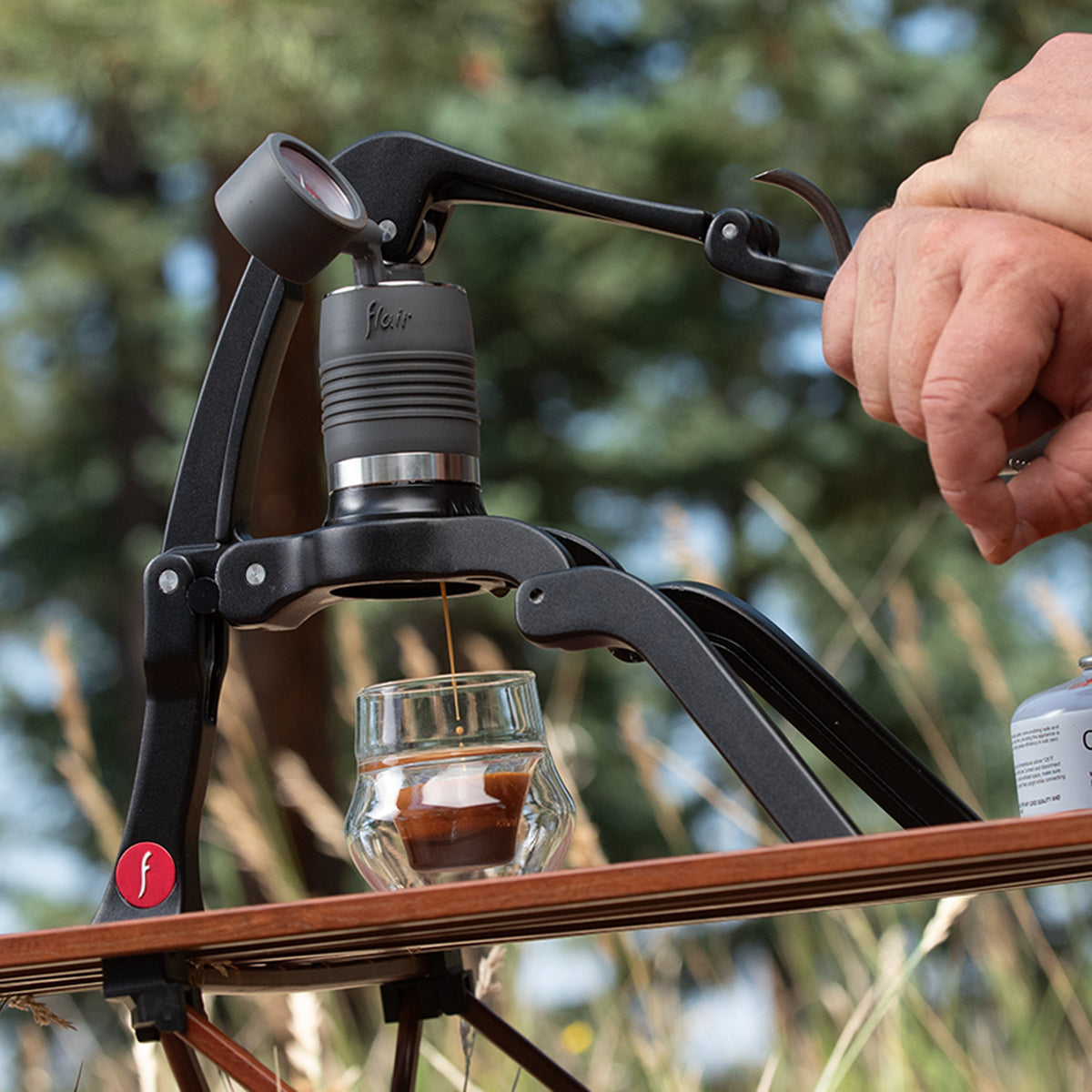 Hand using the Flair 2GO portable espresso maker with a blurred natural background
