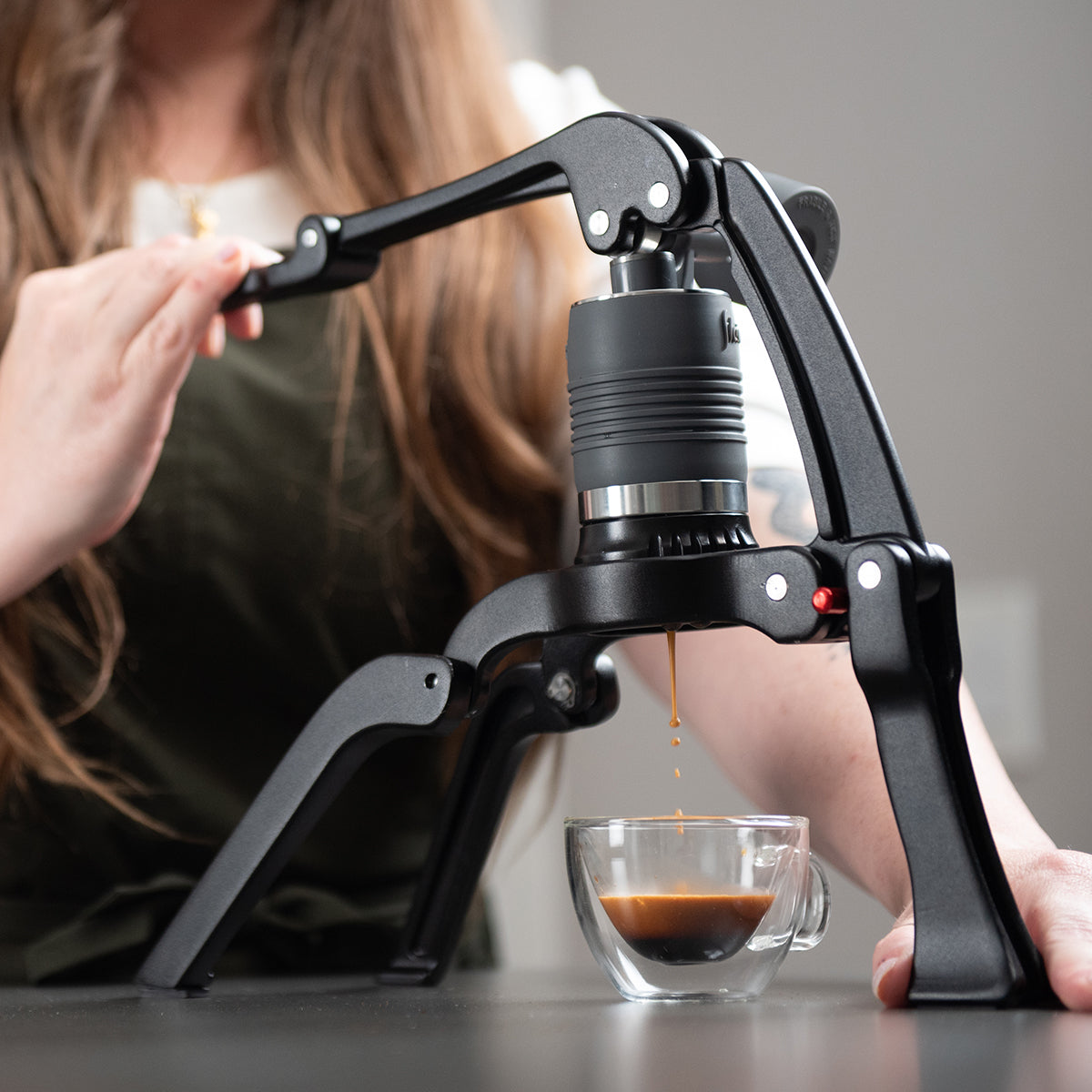 Manual coffee grinder dispensing coffee into a glass cup.