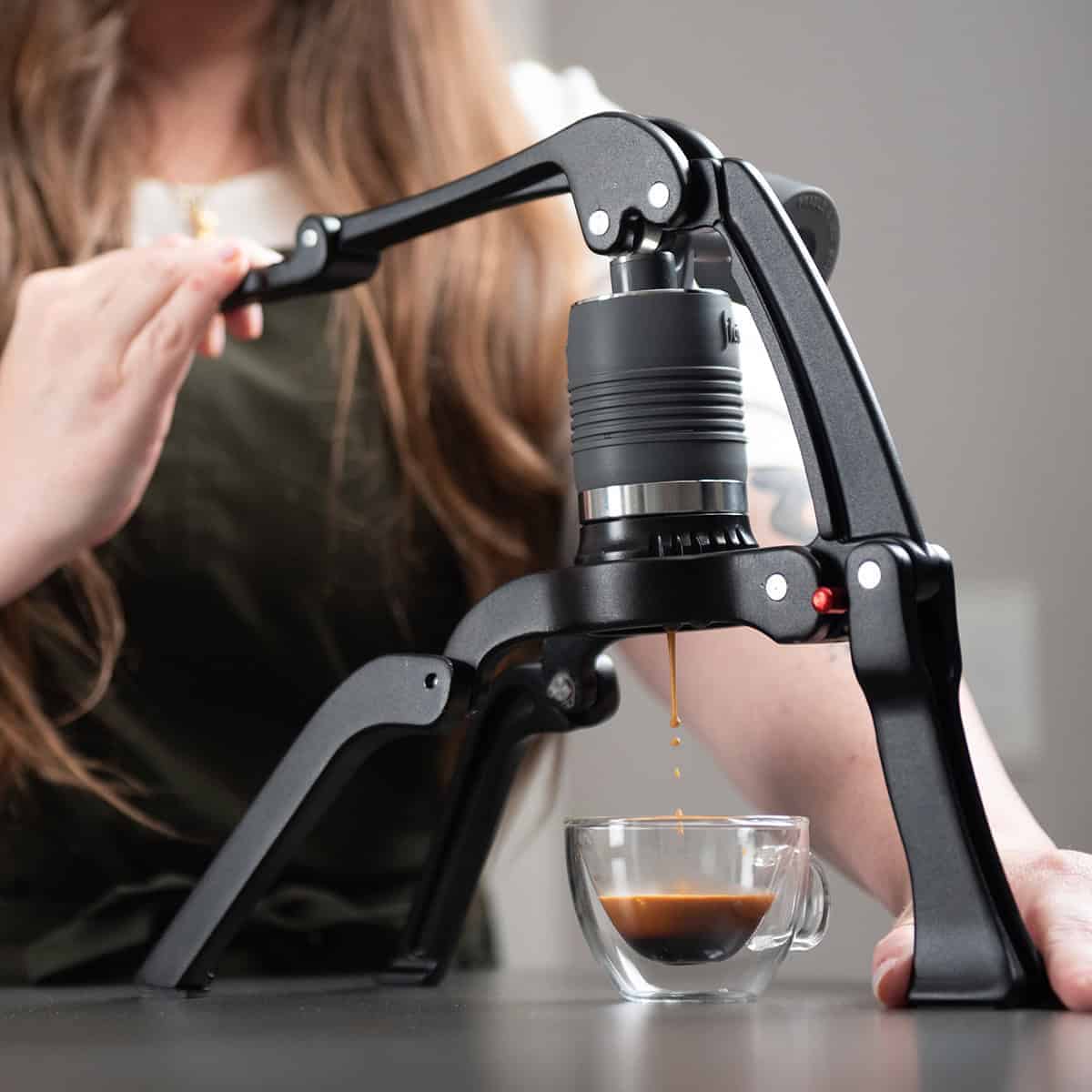 Flair 2GO manual espresso maker with a woman brewing espresso in a kitchen.