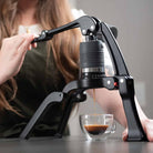 Flair 2GO manual espresso maker with a woman brewing espresso in a kitchen.