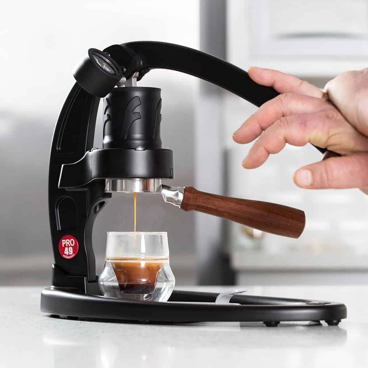 Black Flair 49 PRO manual espresso maker brewing espresso on a counter. Hands on the lever.