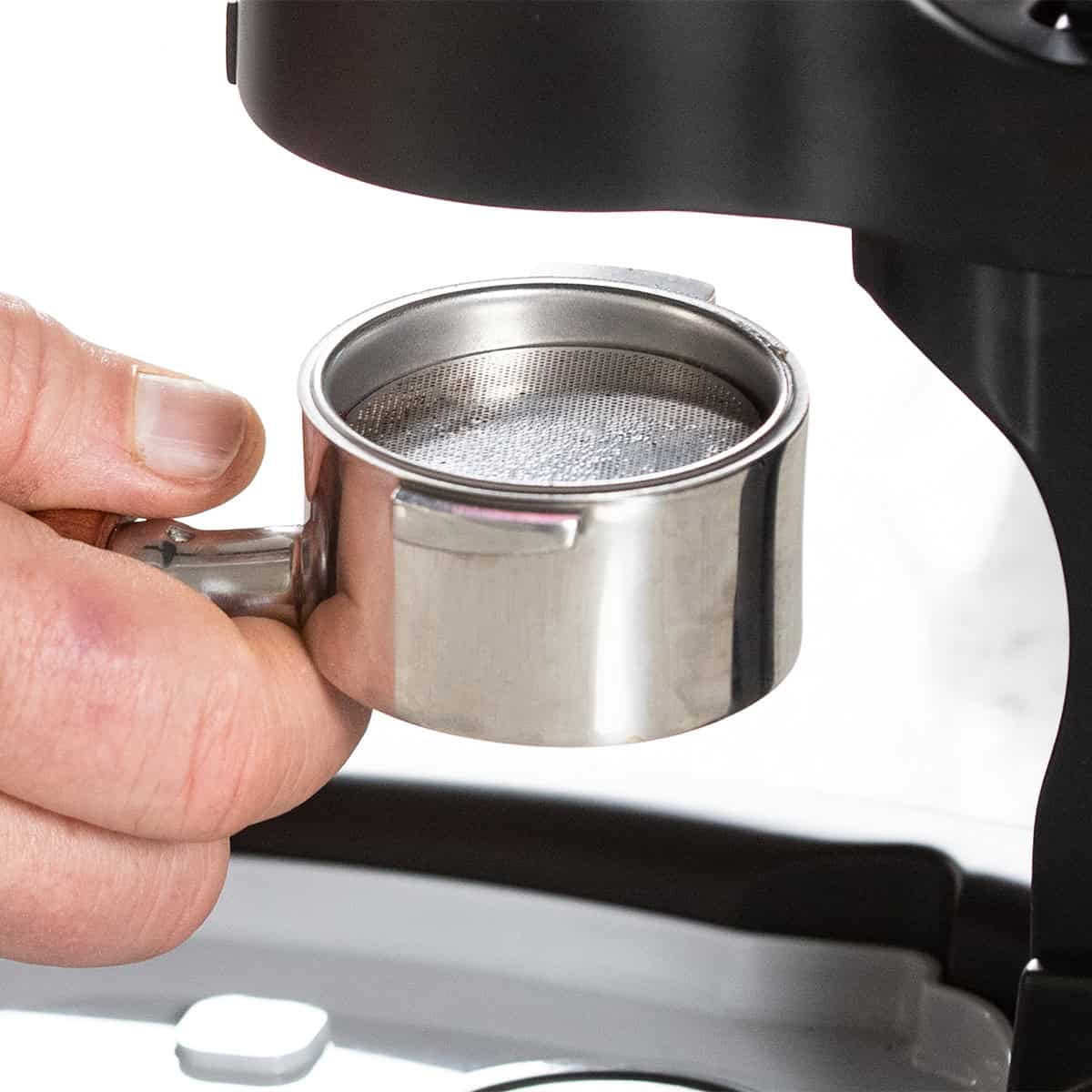 Hand holding a metal coffee filter over an espresso machine.