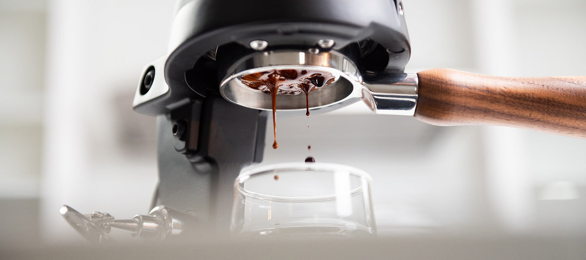 Close-up of an espresso machine with coffee being dispensed onto a reflective surface.