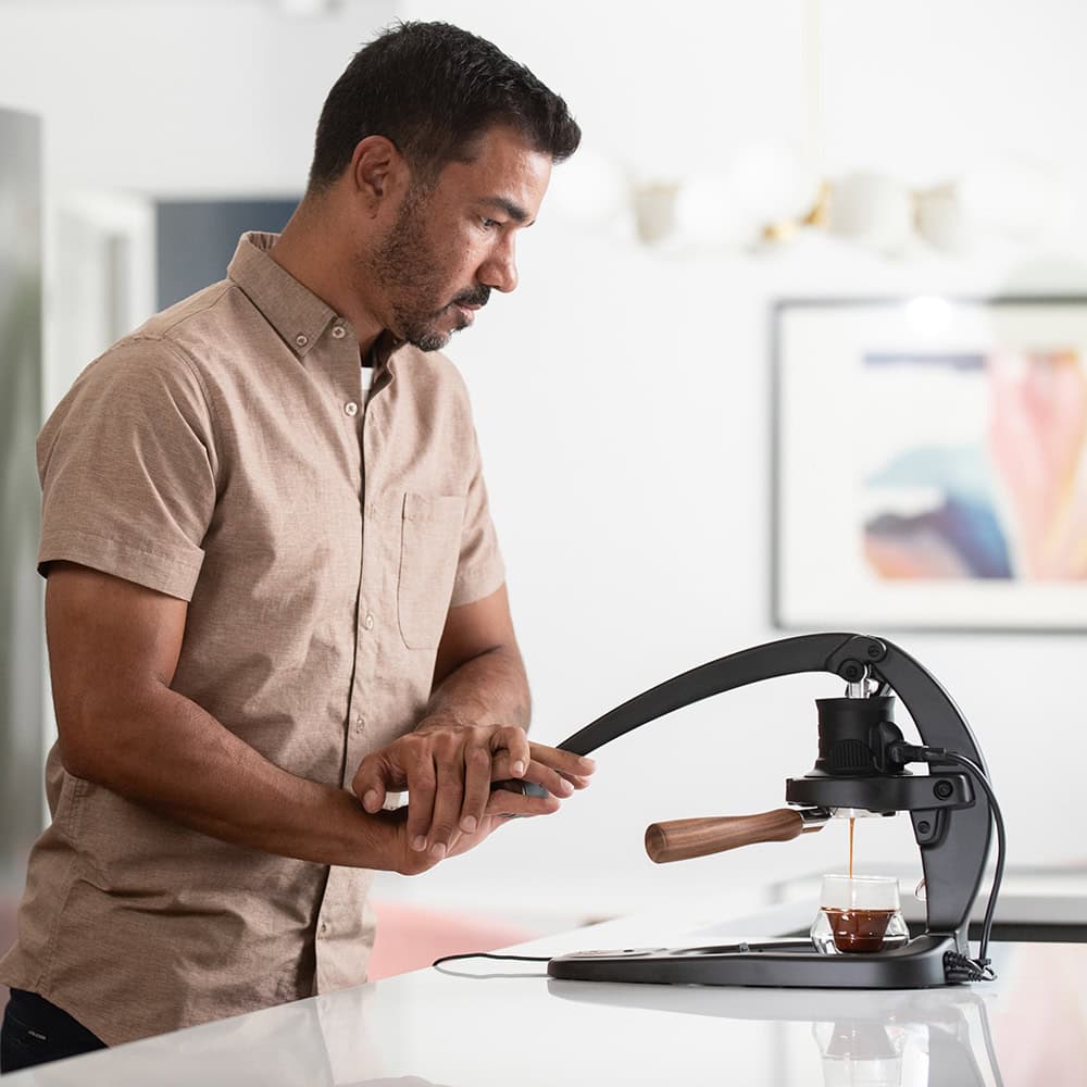 Man using the Flair 58 Plus 2 manual espresso maker on a kitchen counter with a blurred background