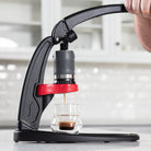 Flair Classic manual espresso machine brewing espresso with hands on the lever in a white kitchen.
