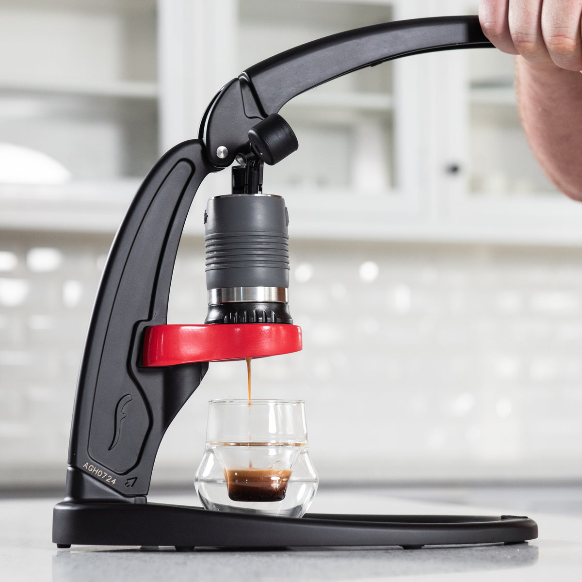 Flair Classic manual espresso machine brewing espresso with hands on the lever in a white kitchen.