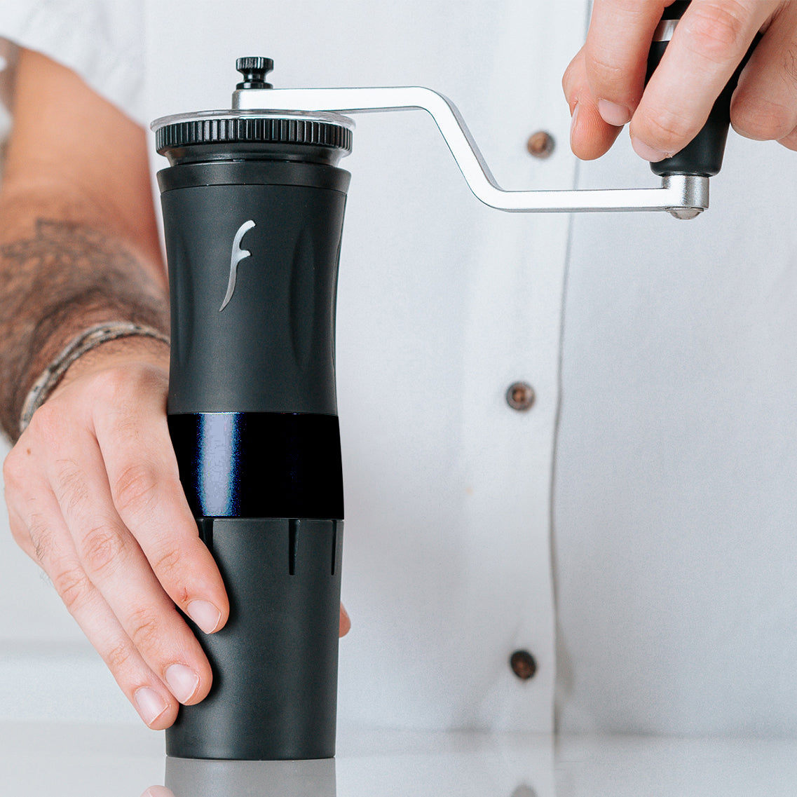 Person using the Flair Royal manual coffee grinder with a visible brand logo on a light background