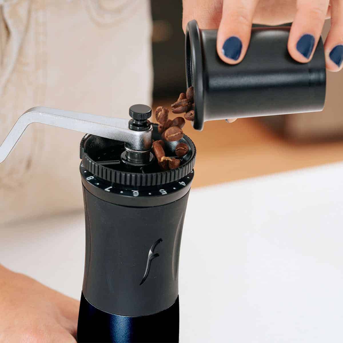 Pouring fresh coffee beans into the top of the Flair Royal hand grinder.