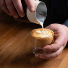 Latte art pouring into a glass cup.
